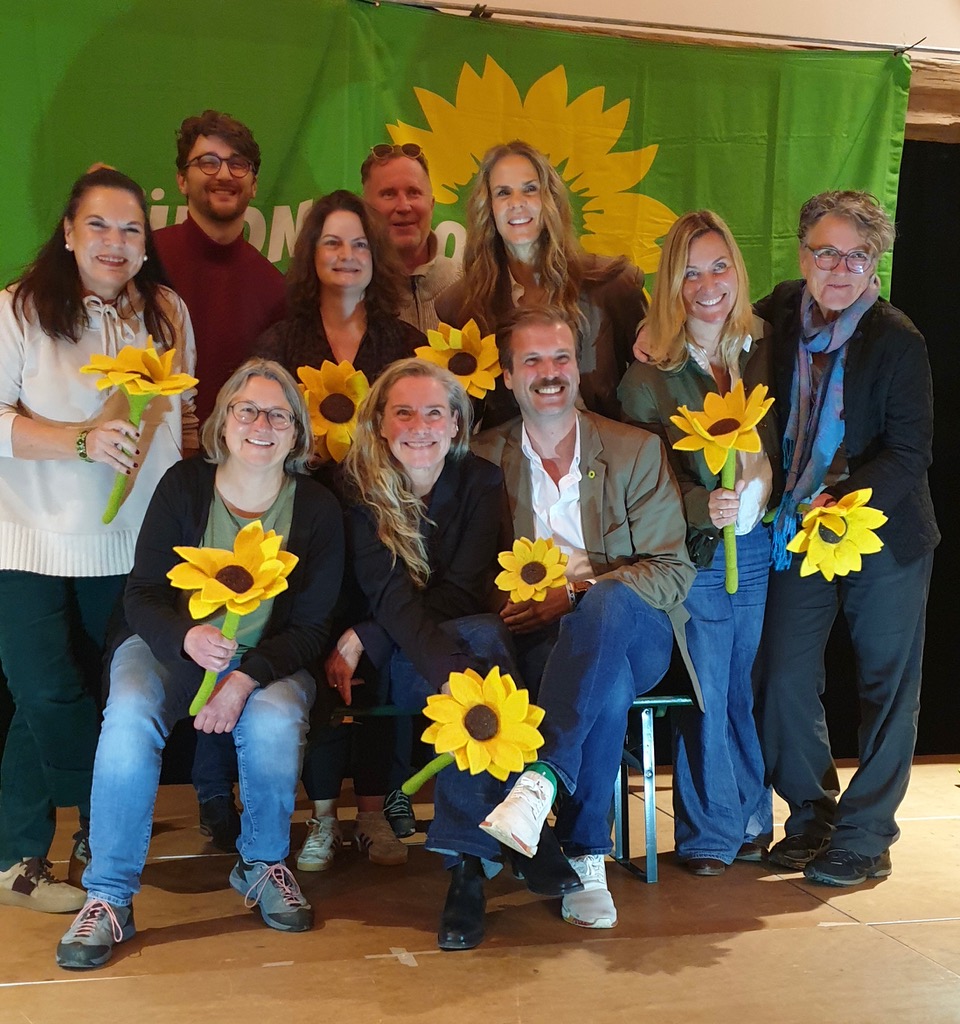 Die neu gewählten Vorstandsmitglieder mit Filzsonnenblumen in der Hand vor einer grünen Fahne mit Sonnenblume im Hintergrund